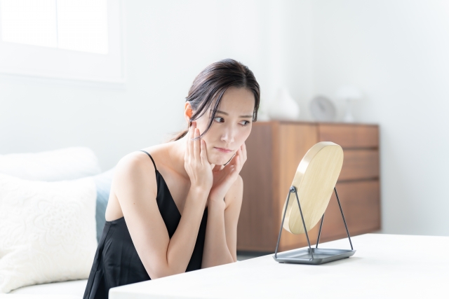 肌のくすみを鏡でチェックしてる女性のイメージ写真